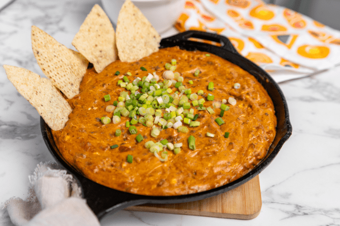 Skillet queso con carne made with seasoned ground beef, melted cheese, diced tomatoes with green chiles, and taco seasoning, garnished and served with tortilla chips
