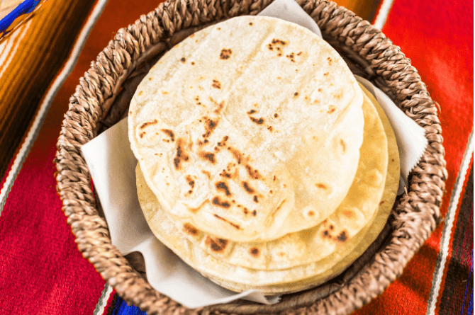 Stack of warm corn and flour tortillas in a woven basket, lightly charred and ready to serve