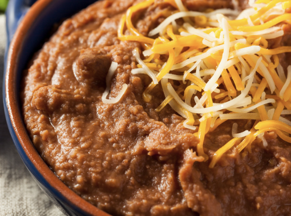 Creamy refried beans in a skillet with a wooden spoon, ready to serve as a side dish or taco filling.